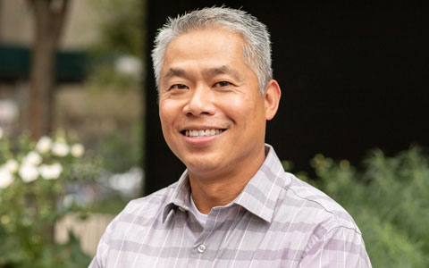 Joseph Kong smiling in a plaid shirt outside.