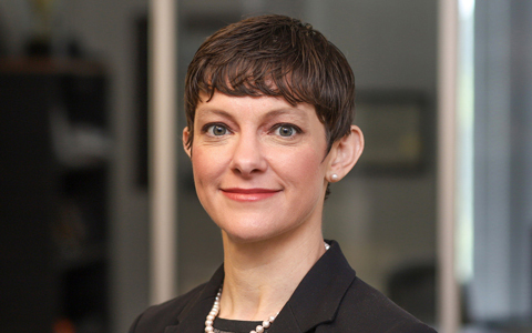 Kate Lindekugel in the office, wearing a dark suit and smiling. 