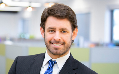 Ken Donald smiles in the office, wearing a blue striped tie and dark suit.