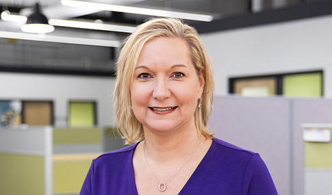 Kirsten Tynch smiles at the camera wearing a purple shirt. 