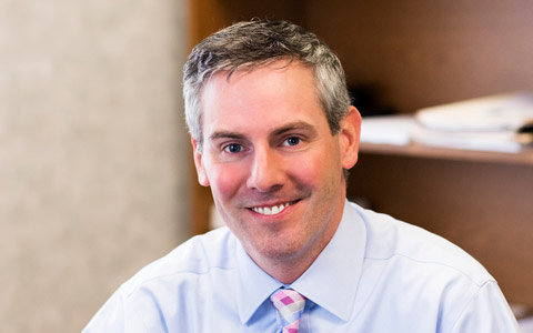 Headshot of Michael Petrin wearing business clothing and smiling with an office background. 