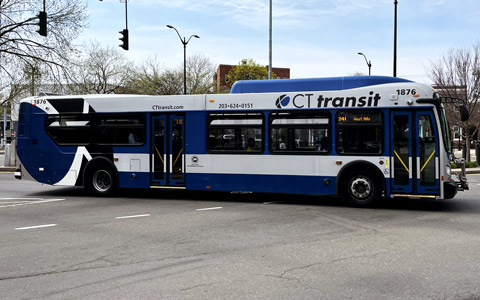 A bus stop sign with a CTtransit bus in the background on the other side of the street.