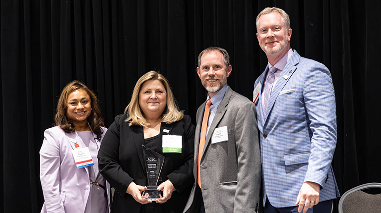 Michelle Cavucci and Dan Lovas stand on stage at the ACEC MW conference to receive the Member Firm of the Year award. 