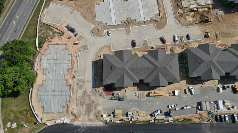 Construction progress shows two completed apartment buildings, parking lot, and the future location of two more buildings.