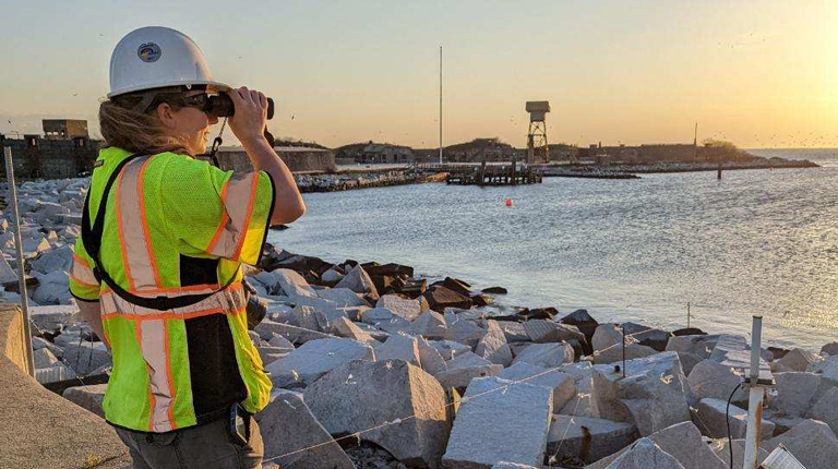Anna Romano looks through binoculars as she bird monitors during a site visit.