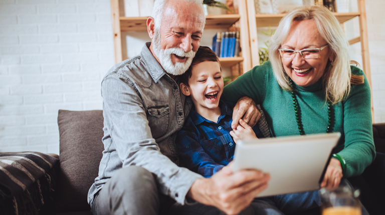 Young boy and grandparents sitting on couch looking at tablet.