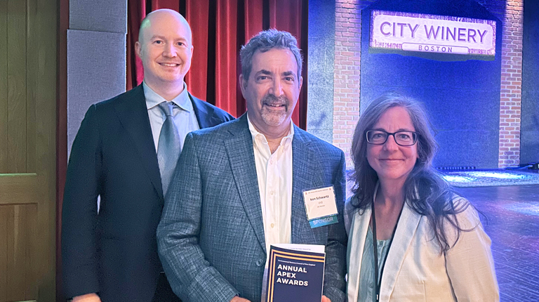 Three individuals stand on stage at City Winery, smiling with one person holding an 'EBC Annual Awards' program.