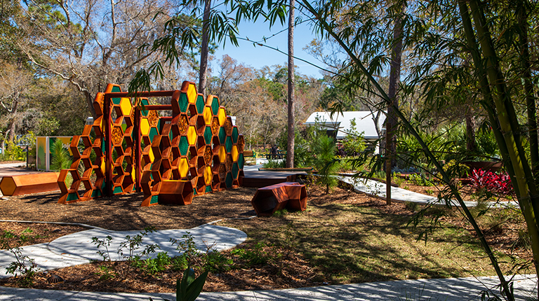 Nature path through bamboo with orange hexagon bench in foreground.