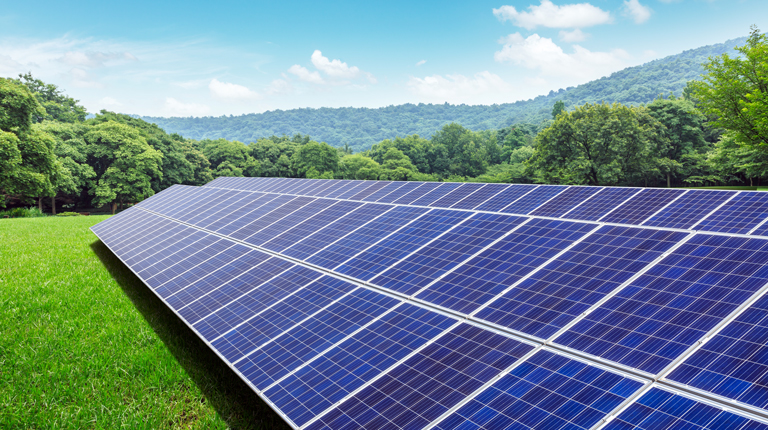 Solar panels and mountains in green grass field.