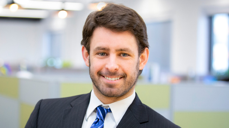 Ken Donald smiles in the office, wearing a blue striped tie and dark suit.