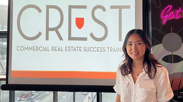 CREST Intern, Lily Liu stands in front of the CREST sign wearing a white top and maroon skirt