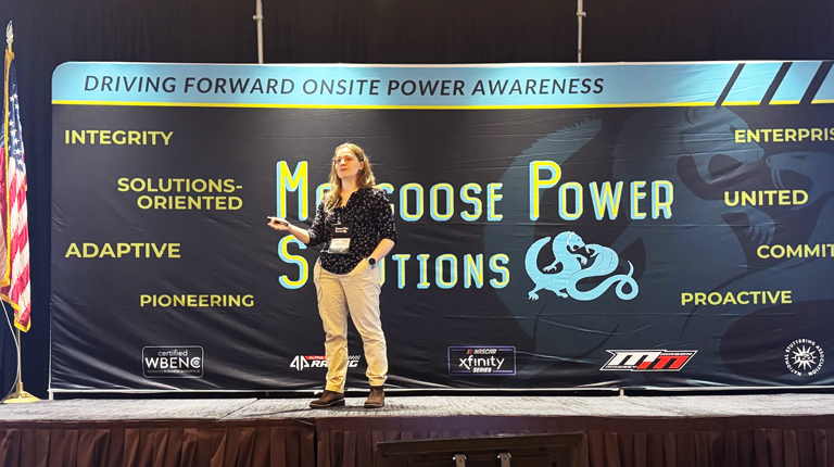 Person presenting on a podium with a banner reading "Mongoose Power Solutions" visible in background.