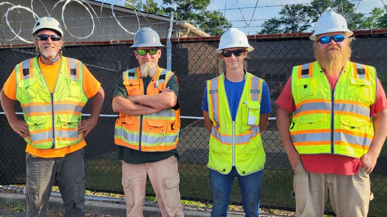 Four men stand together in safety vests preparing to perform rail survey.