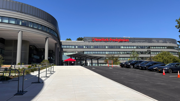 A hospital building with cars parked in front of it.