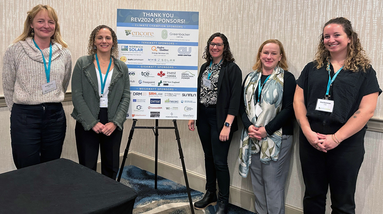 VHBer stand together wearing business attire in front of a sign thanking the 2024 REV Conference sponsors. 