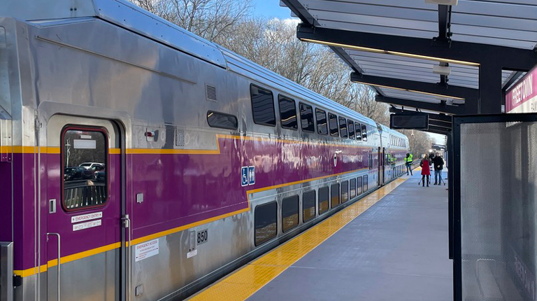 A purple and gray MBTA commuter train at a modern station.