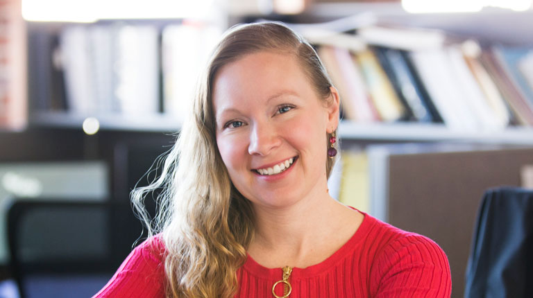 A blonde woman in a red shirt, sitting at a table.