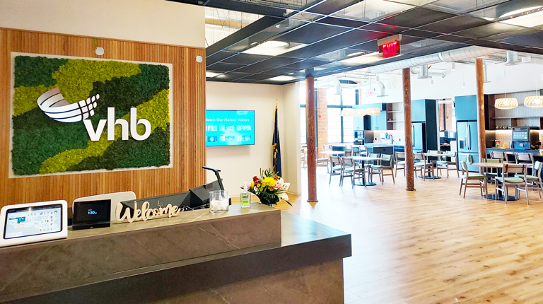 VHB logo on moss sign mounted over reception desk, adjacent to café area with bright windows.