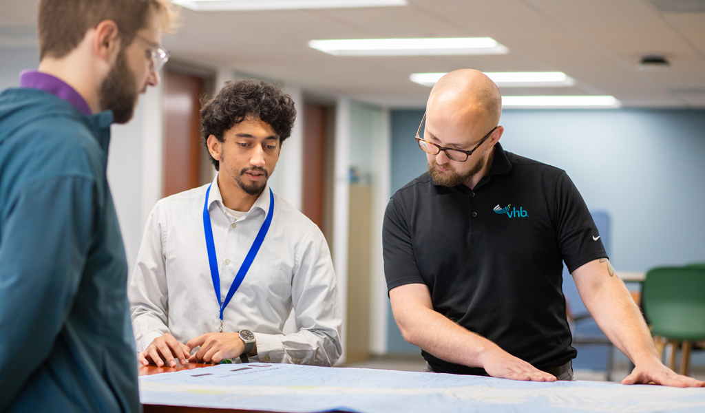 Adrian discusses plans on a table with co-workers.