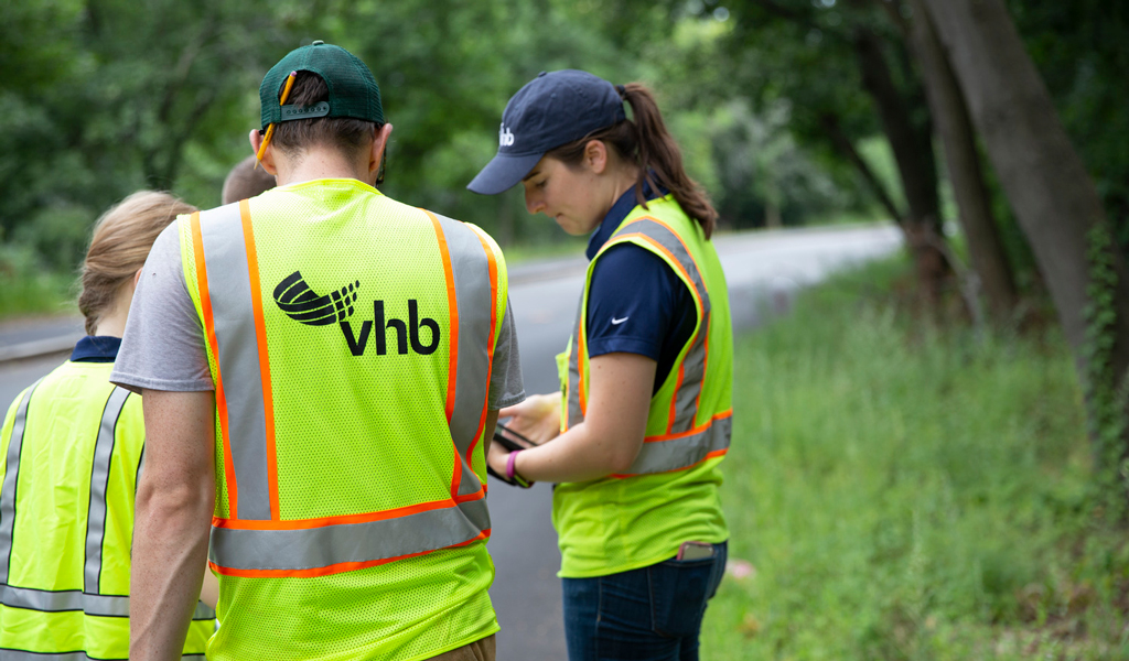 Workers in VHB branded high visibility vest standing on the side of a road.