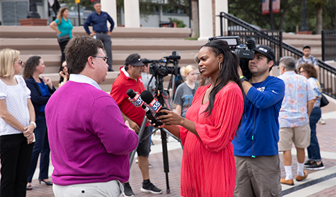 A television reporter holds a microphone and interviews Frank Mertz.