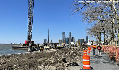 A waterfront construction site with a crane and a city in the background