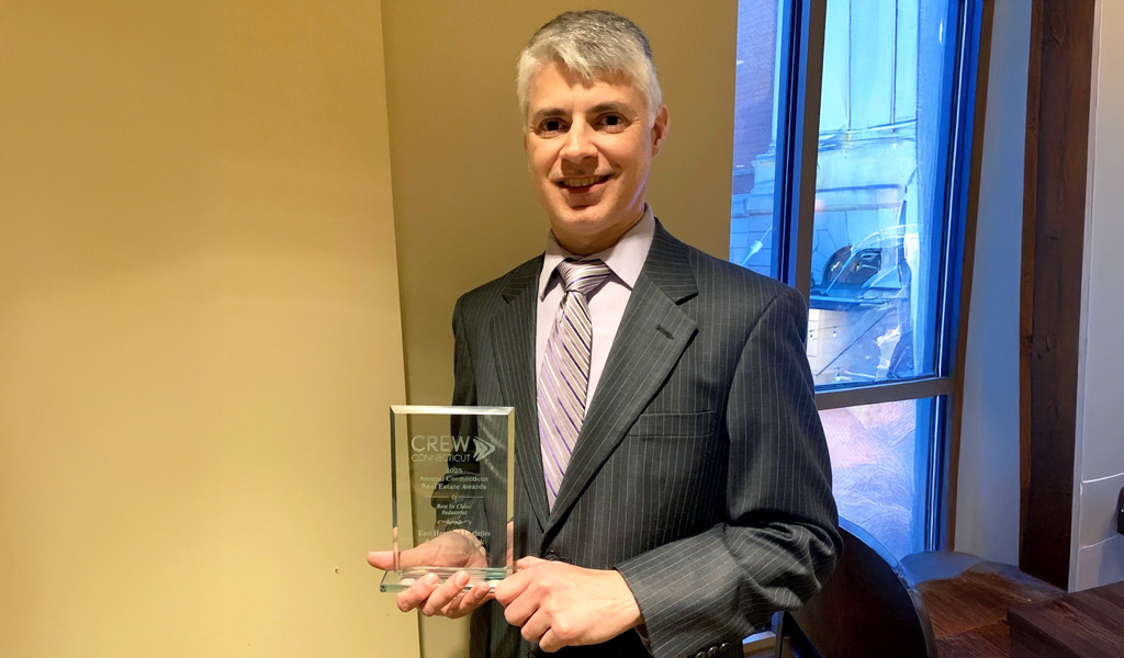 Person holding a CREW Network award, wearing a suit and tie, smiling in an indoor setting.