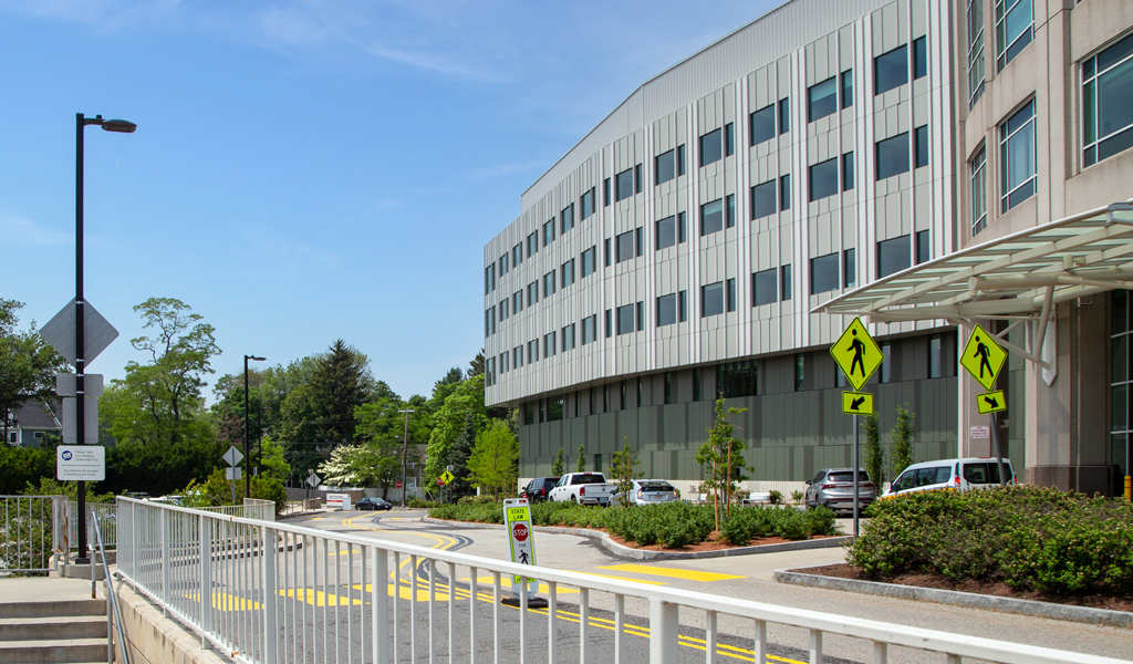 A five-story hospital with surrounding parking and a stairway to public transit station.
