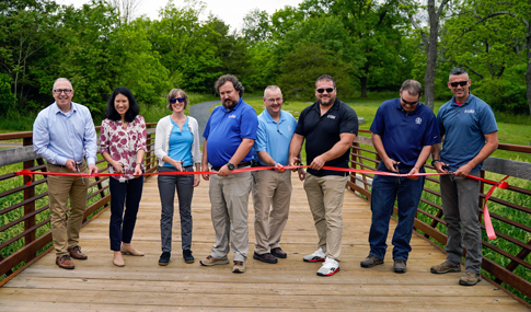 Eight individuals stand together to cut a red ribbon during the grand opening of the Friendly City Trail