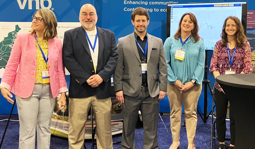 Five professionals standing at a VHB exhibition booth at a conference.