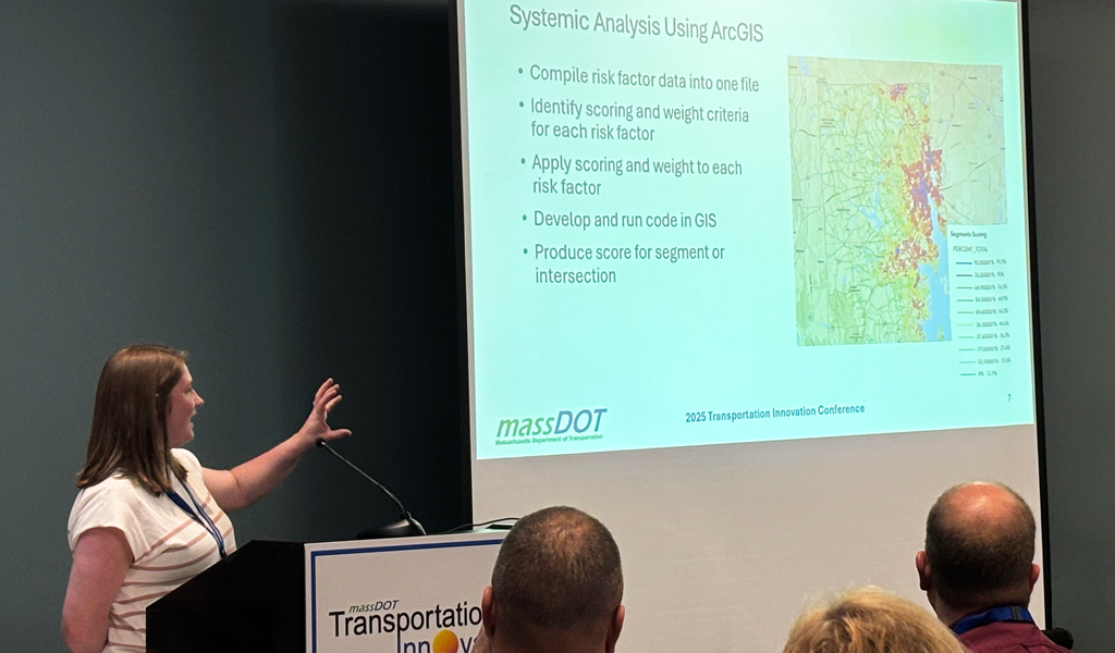 A person stands next to a screen with a list of bullet points about project management and road maintenance statistics.