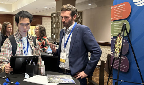 Matt Duranleau talks with a conference attendee at the VHB booth while looking at an iPad. 