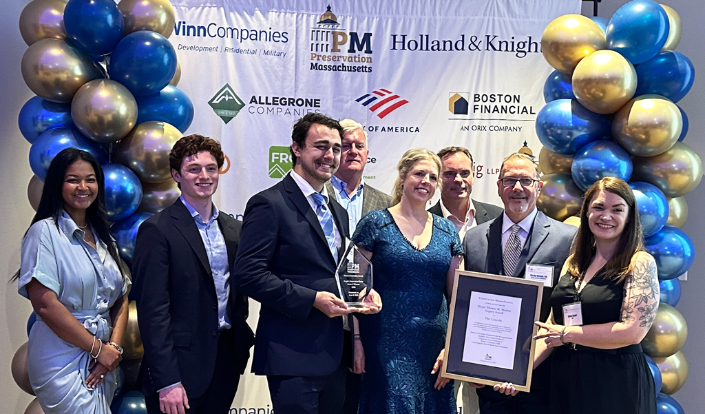 Group of people posing with an award at an event sponsored by WinnCompanies and others, standing in front of a balloon backdrop with company logos.