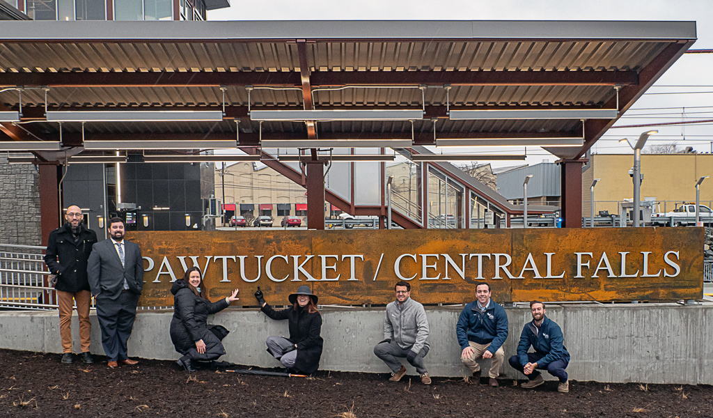 Group of people in front of a metal sign.