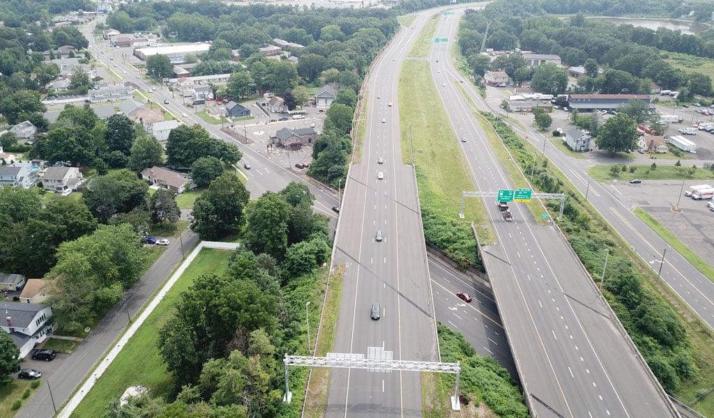 A highway shown from above, with industry and trees shown behind it.