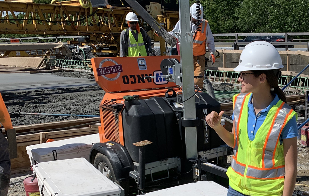 Olivia Richards in safety gear surveying a construction site with fresh concrete and two men in the background