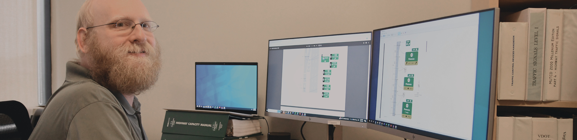 Michael Tantillo in a green shirt work on traffic signage designs across three computer screens.