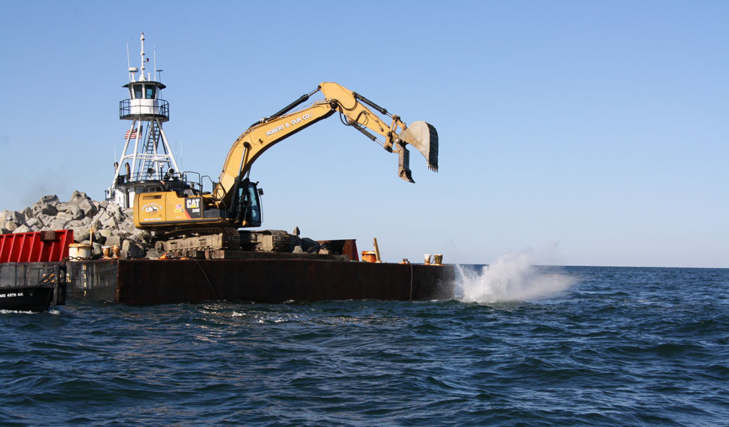 A backhoe dropping granite blocks into a new fish habitat reed.