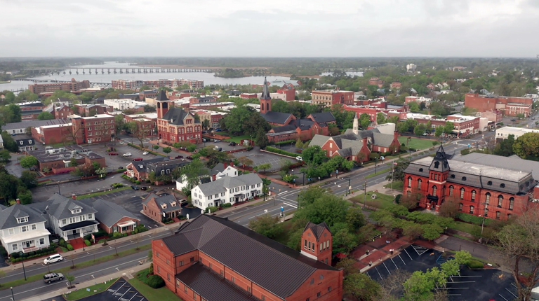 An aerial view of the downtown area of New Bern, NC, with green space and many brick buildings.